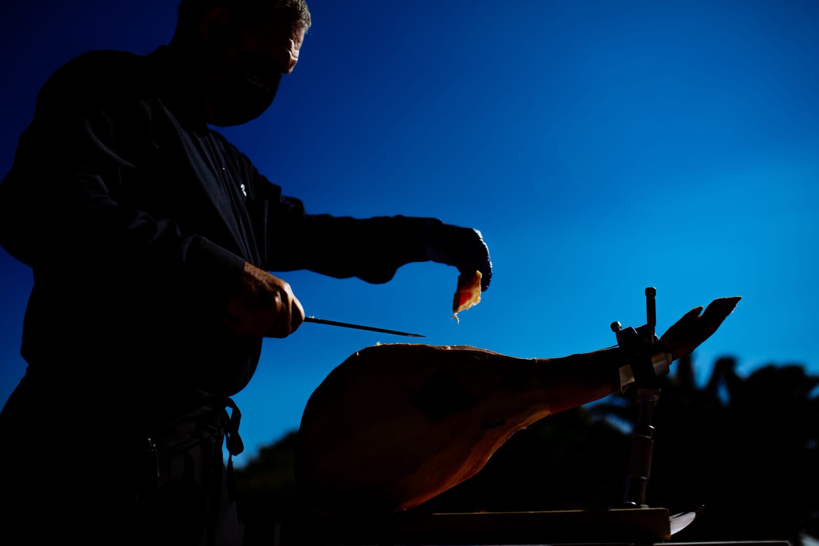 Cortador de jamón en silueta perfilando un jamón de Teruel al atardecer